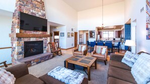 A spacious living room with a stone fireplace, comfortable seating, and a kitchen area in the background. - Red Barn of Granby Ranch - spacious luxury, pet friendly and hot tub (Granby)