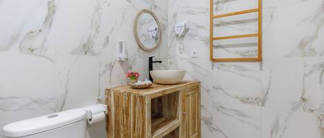 A bathroom with a toilet, a wooden vanity with a bowl sink, a mirror, a towel rack, and a marble wall.