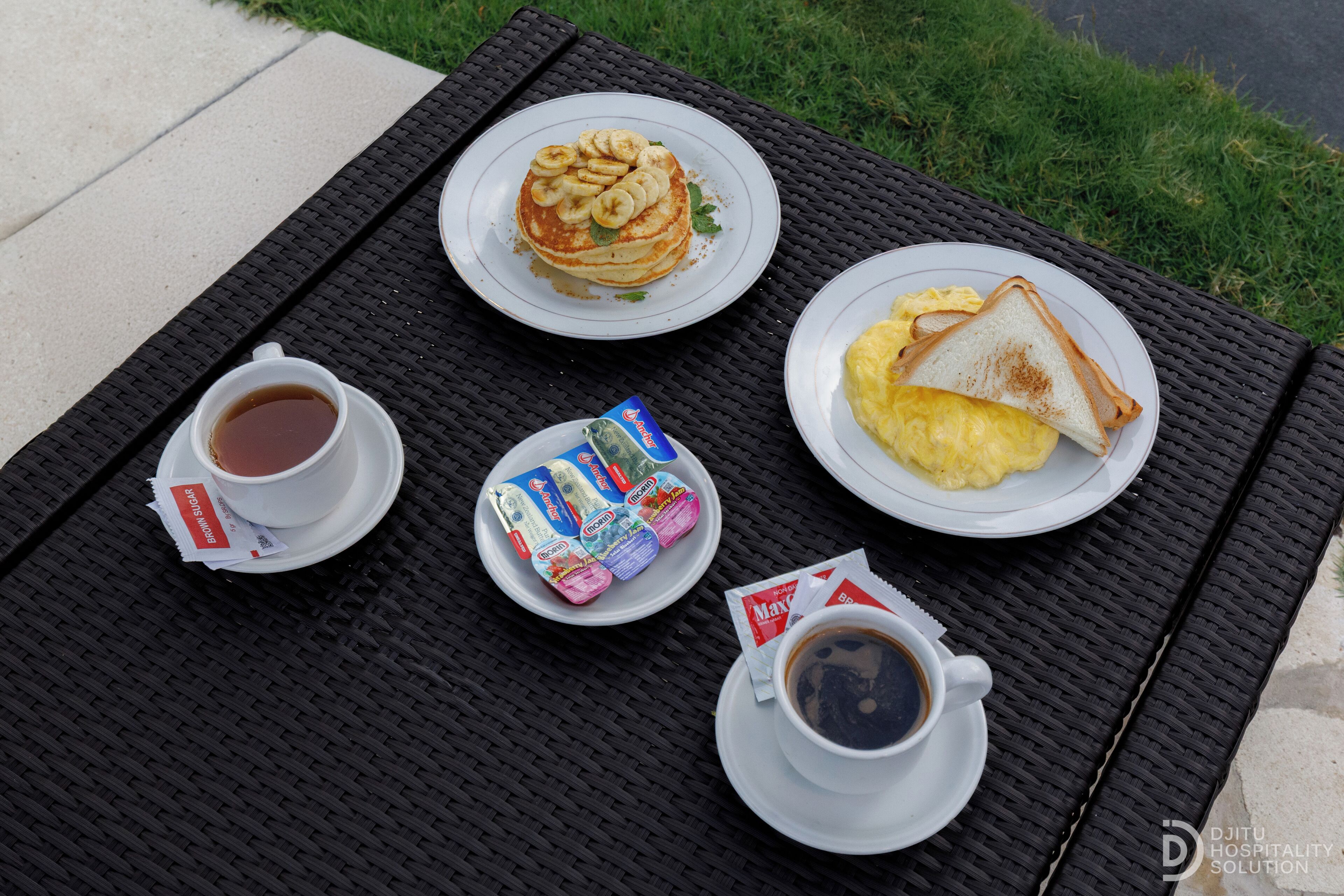 A breakfast setup on a woven table with pancakes, toast, coffee, and a newspaper.