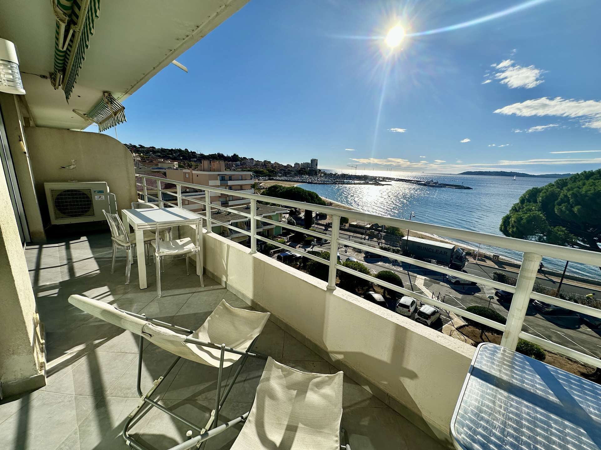 A balcony with a table and chairs, overlooking a waterfront with buildings and a clear sky.