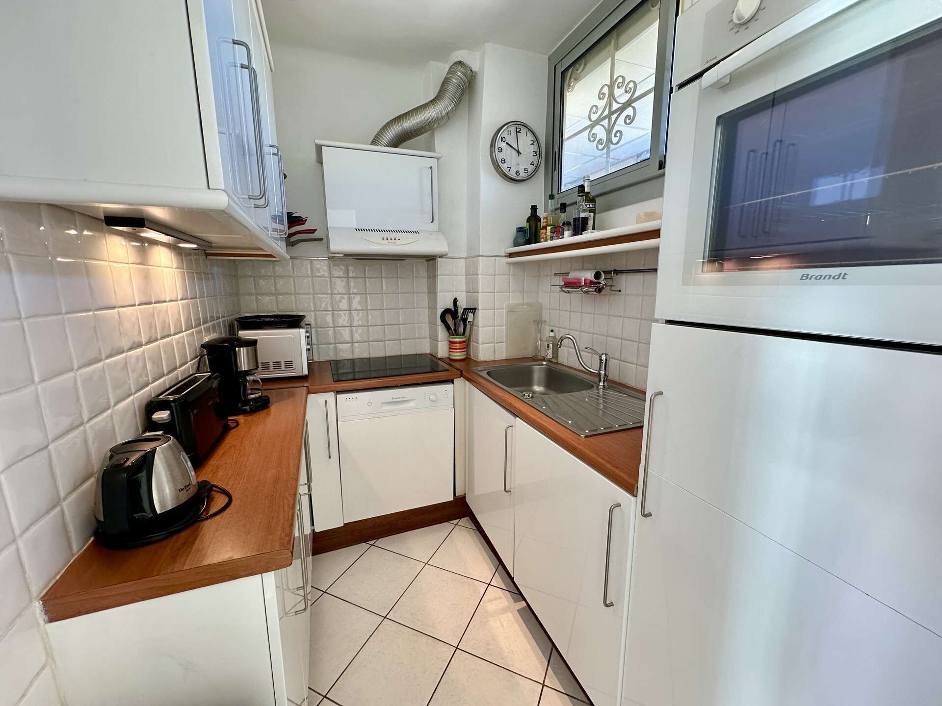 A compact kitchen with white cabinets, a built-in oven, a sink, and a clock on the wall.