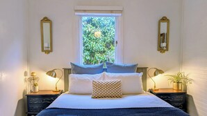A neatly arranged bedroom with a large bed, two bedside tables with lamps, a window with a view of greenery, and two wall-mounted mirrors. - The Wildflower Cottage - 5 minutes to the heart of the Blue Mountains (Katoomba)