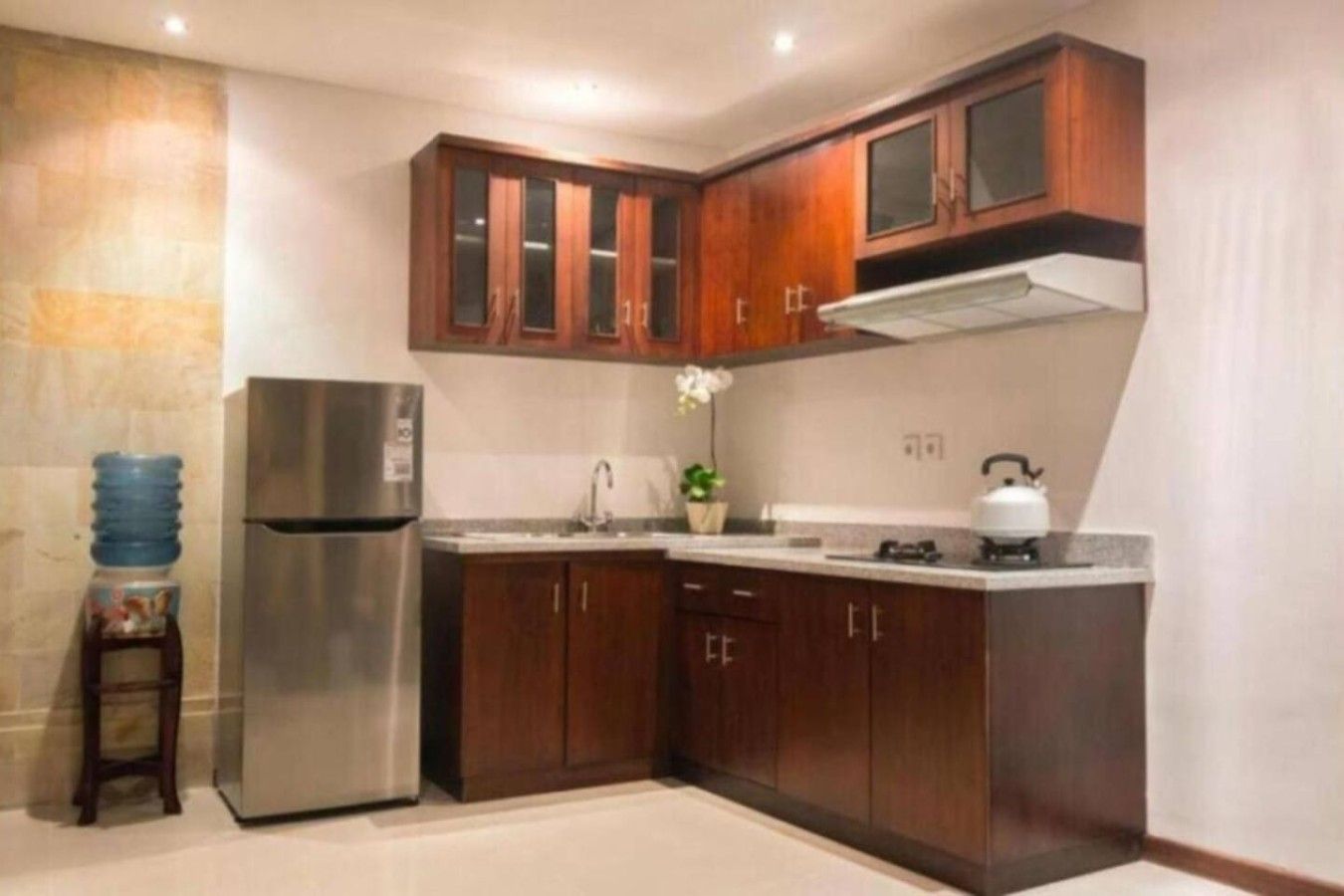 A compact kitchen with dark wooden cabinets, a stainless steel refrigerator, a gas stove, and a water dispenser.
