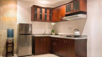 A compact kitchen with dark wooden cabinets, a stainless steel refrigerator, a gas stove, and a water dispenser.