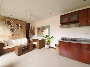 A modern living room with a sofa, a coffee table, and a dining area with wooden cabinets and a stove.