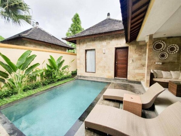 A pool area with lounge chairs and a stone building with a door.