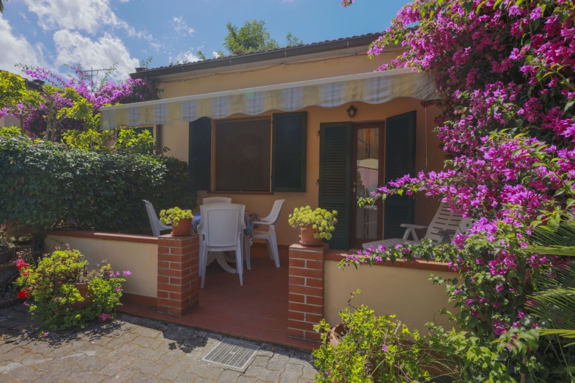A small house with a patio, two white chairs, and a table.