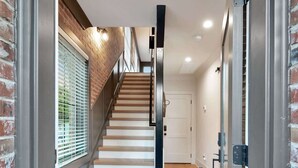 Una entrada de hotel moderna con una escalera de madera, un marco de puerta metálico y un felpudo.