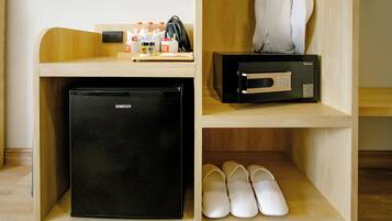 A compact kitchenette with a black refrigerator, a microwave, and a small shelf with slippers and toiletries.