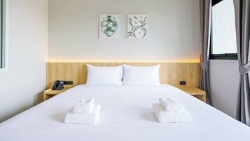 A hotel room with a large bed, two pillows, a bedside phone, and two towels on the bed.