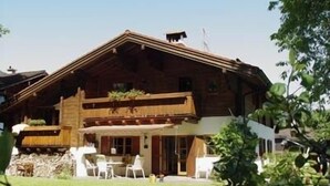 Een houten chalet met een balkon, een eethoek met stoelen en een kleine tuin.