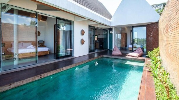 Une maison moderne dotée d’une piscine, de portes vitrées donnant accès à une chambre et d’un petit espace extérieur aménagé pour se détendre.