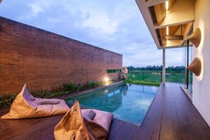 Un área de piscina moderna al aire libre con pared de ladrillo, una estatua y un muelle de madera.