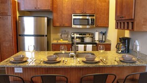 Cocina con armarios de madera, electrodomésticos de acero inoxidable y encimeras de granito, además de asientos de bar.