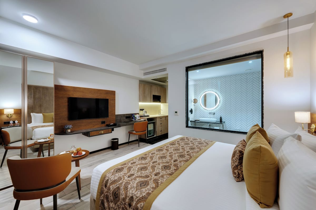 Habitación de hotel con una cama grande, un área de descanso con una silla, un escritorio, un espejo y un televisor.