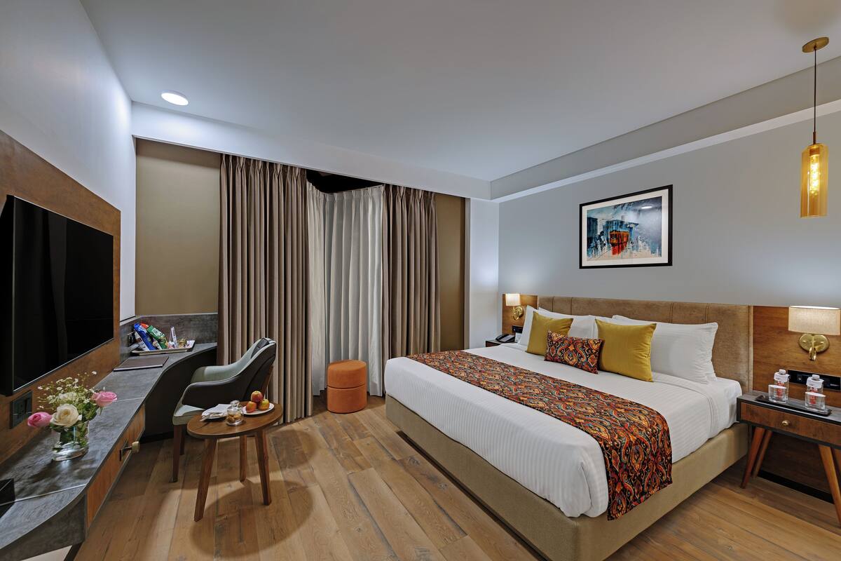 Habitación de hotel con una cama grande, un escritorio con silla, un televisor y un cuadro en la pared.