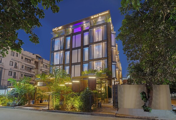 A modern hotel with multiple floors, large windows, and a well-lit entrance area with plants and a fence.