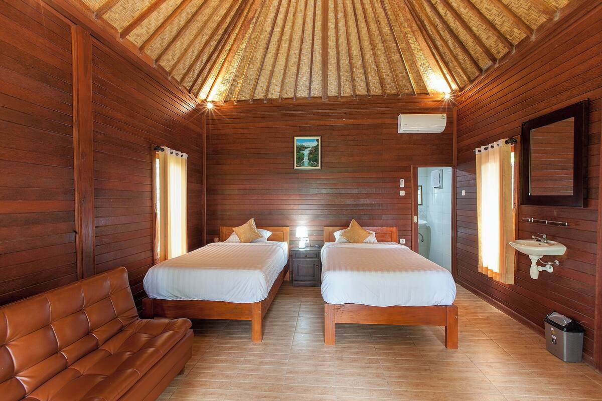 A wooden cabin room with two beds, a sofa, a small table, a sink, and a picture on the wall.