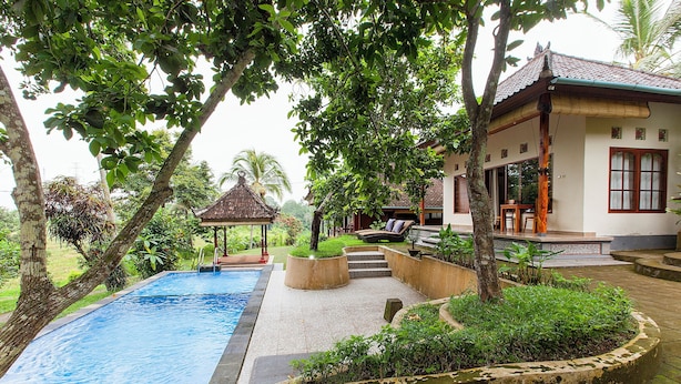 A swimming pool surrounded by greenery, a gazebo, and a building with a tiled roof. - Pondok Hari Baik (Selemadeg)