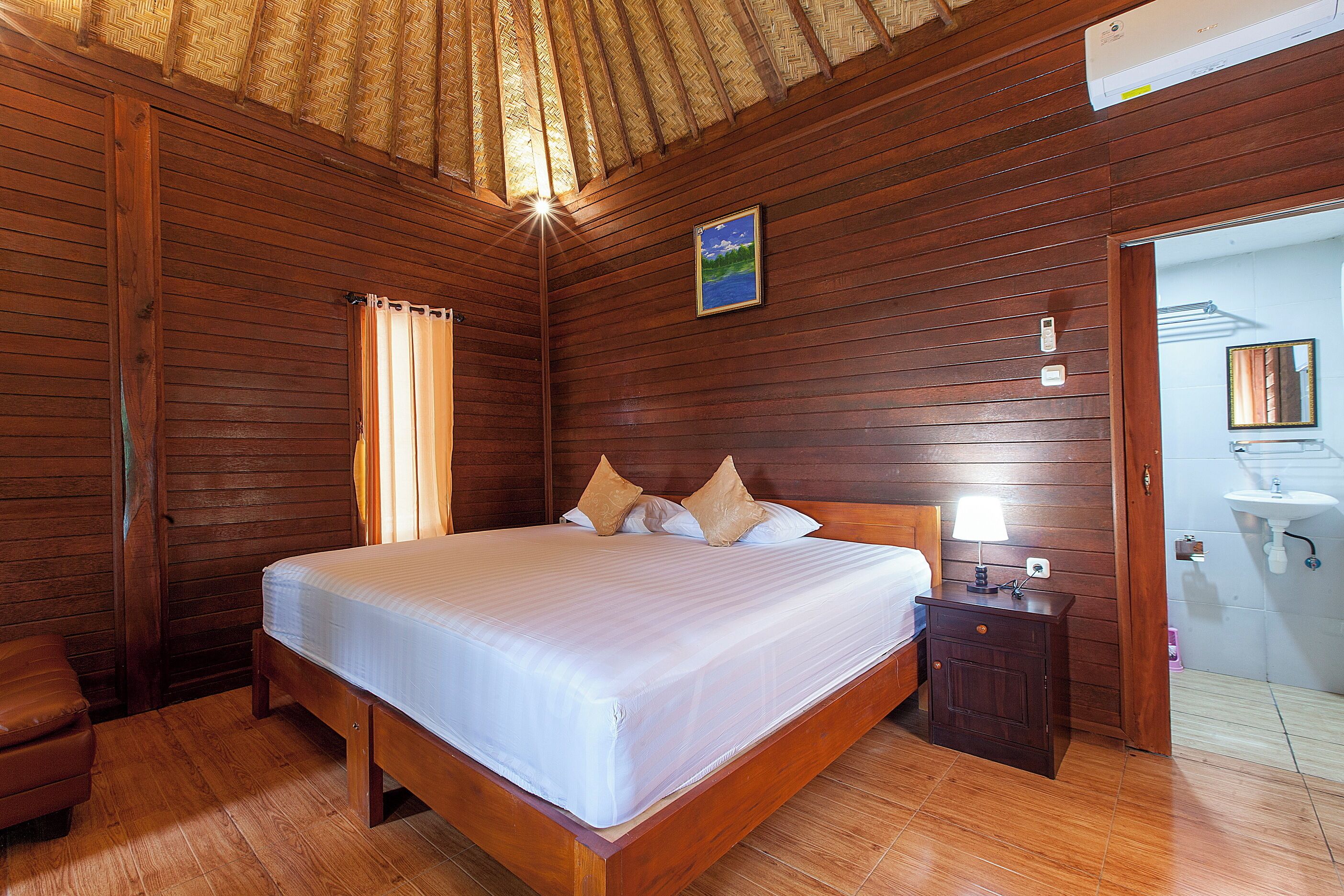 A wooden-paneled room with a bed, a nightstand, and a bathroom visible through an open door.