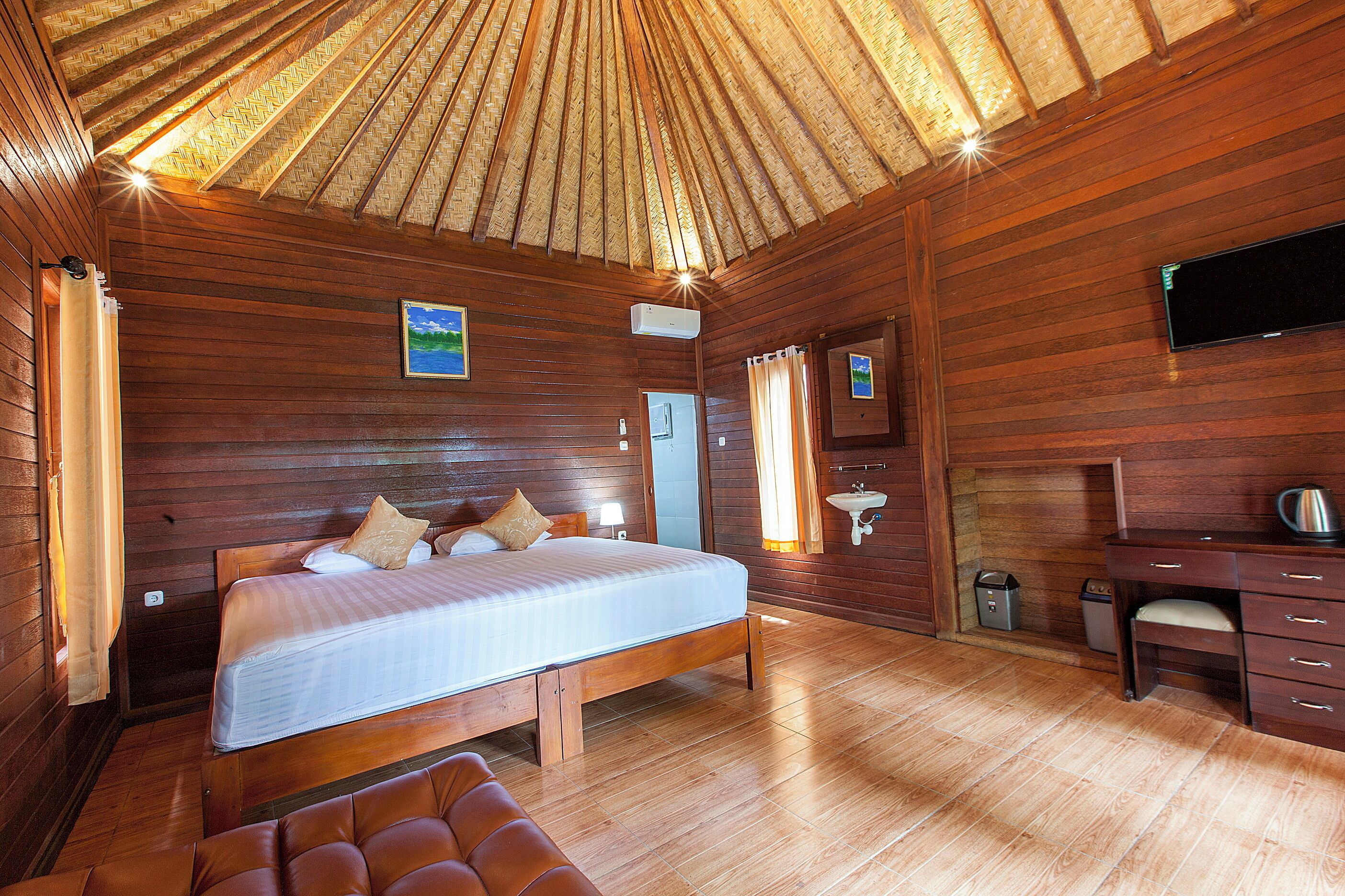 A wooden cabin bedroom with a bed, a desk, and a television.