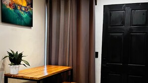 A room with a wooden table and bench, a potted plant, a black door, and a painting on the wall.