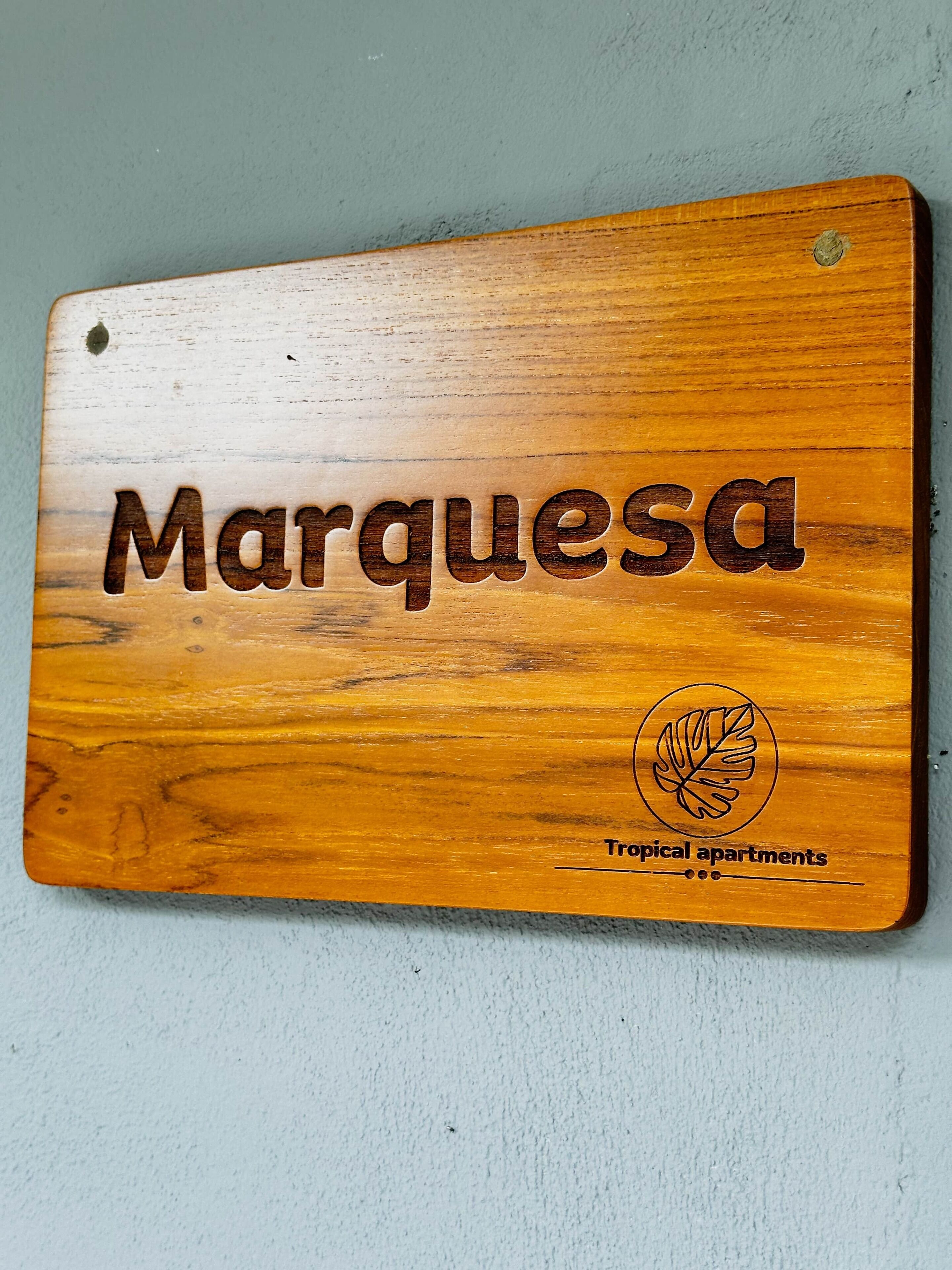 Eine Holzplakette mit dem Wort 'Marquesa' und einem Logo für 'Tropical apartments'.