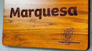 Een houten plaquette met de tekst 'Marquesa' en een logo voor 'Tropical apartments'.