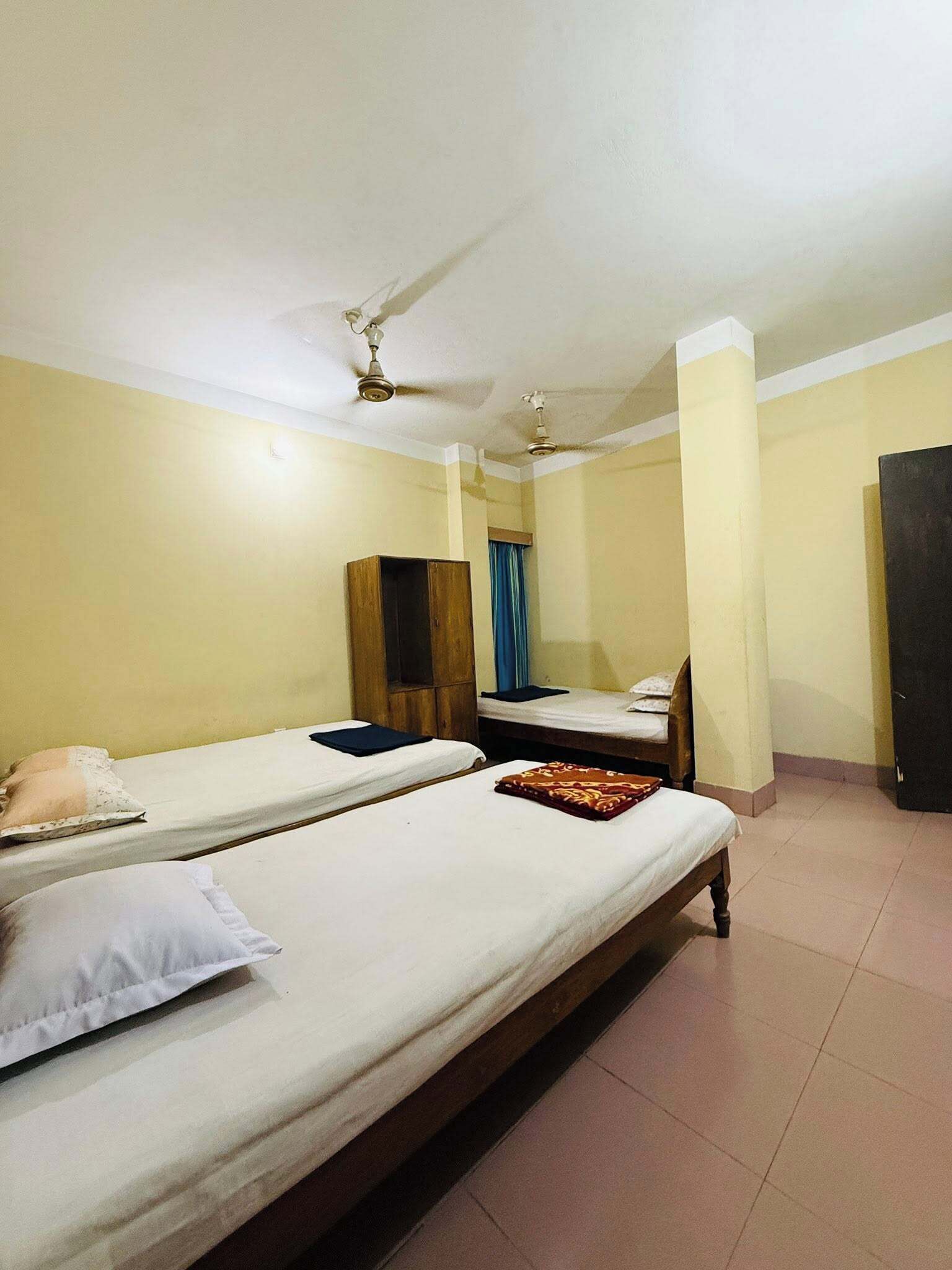 A room with two single beds, a wooden wardrobe, a ceiling fan, and a door.