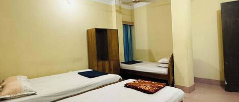 A room with two single beds, a wooden wardrobe, a ceiling fan, and a door.