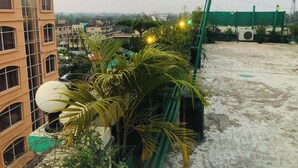 A rooftop with a green crane, palm trees, and a building with multiple windows. - Green View Rest House (Sreemangal)