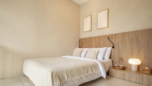 Un dormitorio con una cama grande, cabecera de madera, mesita de noche con lámpara y dos cuadros enmarcados en la pared.