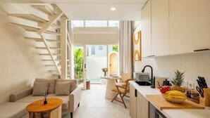 Una cocina moderna con una isla de madera, un comedor con mesa redonda y una escalera que lleva a un espacio al aire libre.