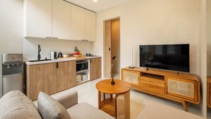Una cocina moderna con armarios de madera, microondas integrado y dispensador de agua. Hay una mesa redonda de madera con un florero y un televisor de pantalla plana sobre un mueble de madera.