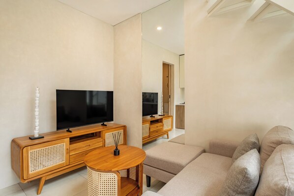 A modern living room with a flat-screen TV on a wooden cabinet, a round wooden table, and a beige sofa.