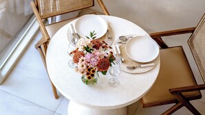 Una mesa redonda con mantel blanco, dos sillas y un florero con flores.