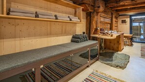 Interior acogedor de una cabaña con un banco, estantes con toallas, una mesa de madera y suelo de piedra.