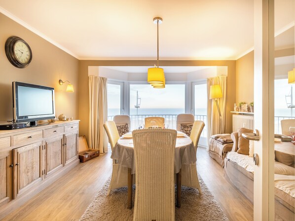 A modern living room with a dining area, a television, and a view of the sea. - Cottage-style apartment with sea view (Koksijde)