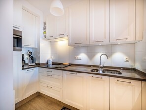 A modern kitchen with white cabinets, stainless steel appliances, and a wooden floor. - Cottage-style apartment with sea view (Koksijde)