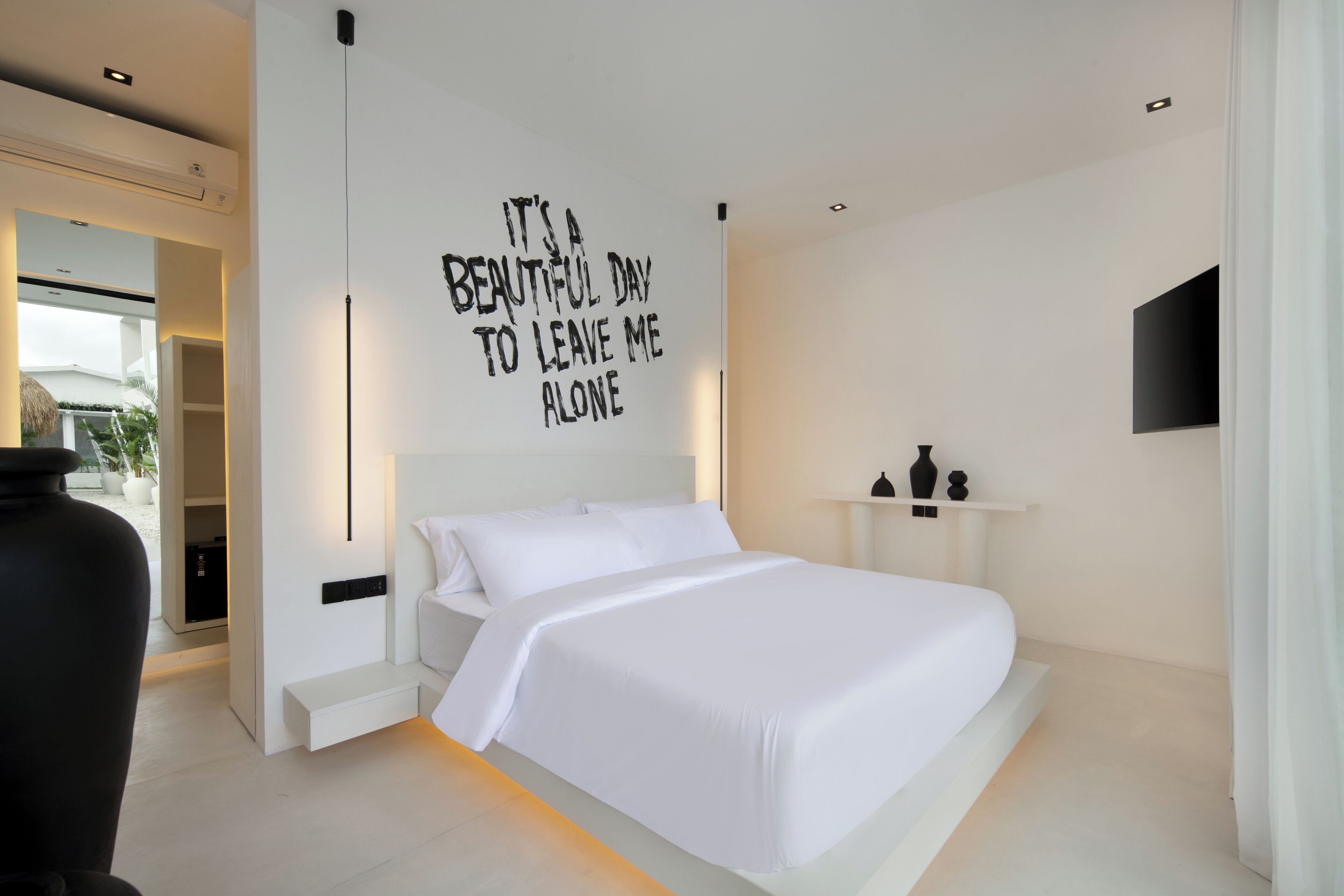 A modern bedroom with a large bed, a wall-mounted TV, and a motivational quote.