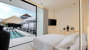 A modern hotel room with a large bed, a TV mounted on the wall, and a view of a pool area with umbrellas and lounge chairs. - the den canggu (Canggu)