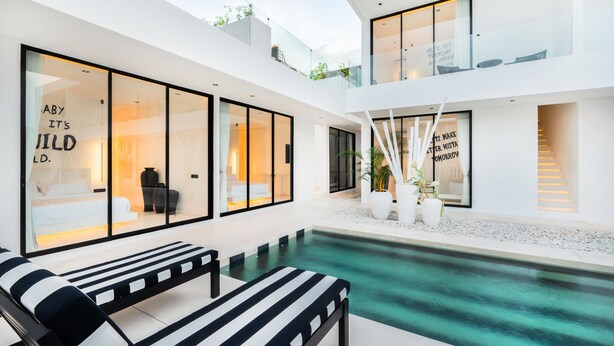 A modern outdoor pool area with lounge chairs, a glass-enclosed room with a bed, and a staircase leading to an upper level. - the den canggu (Canggu)