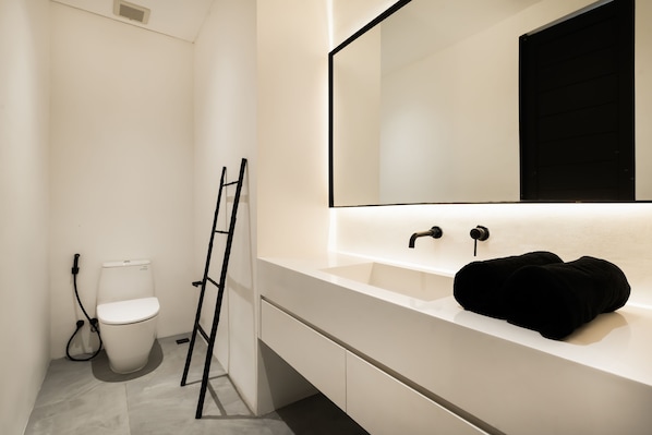 A modern bathroom with a white sink, a black towel, and a toilet. - the den canggu (Canggu)