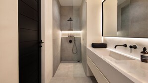 A modern bathroom with a walk-in shower, a large mirror, and a vanity with a sink and soap dispenser. - the den canggu (Canggu)