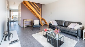 Un salon moderne avec un escalier, un canapé en cuir noir, une table basse en verre et un vase blanc orné de fleurs.