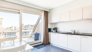 Une cuisine moderne avec des meubles blancs, un plan de travail noir et une vue sur la ville grâce à une grande fenêtre.