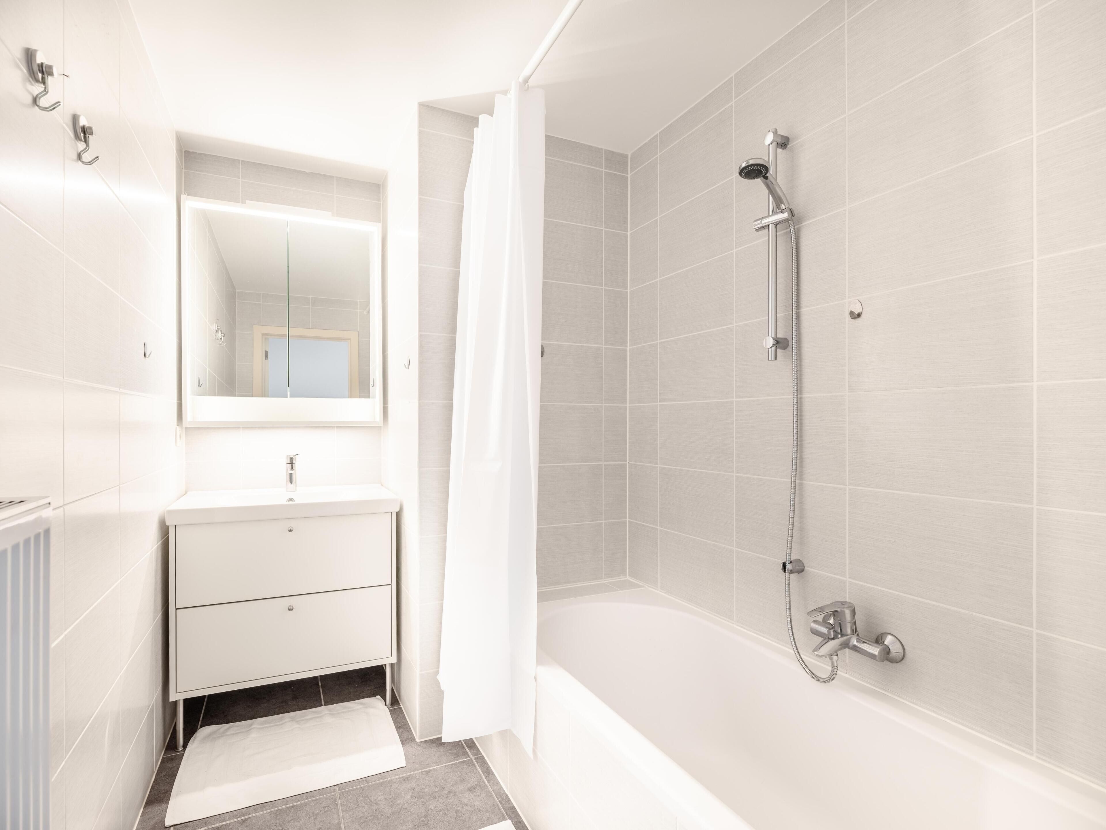A modern bathroom with a bathtub, a shower, a sink, and a mirror.