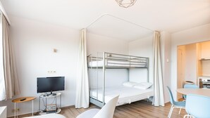 A modern hotel room with a bunk bed, a desk with a computer, a TV, and a dining area with chairs. - Renovated studio with sea views (Oostduinkerke)