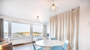 A modern room with a round table, blue chairs, a sofa, and large windows overlooking a beach. - Renovated studio with sea views (Oostduinkerke)