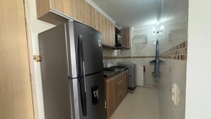A kitchen with wooden cabinets, a stainless steel refrigerator, a stove, and a mop leaning against the wall.